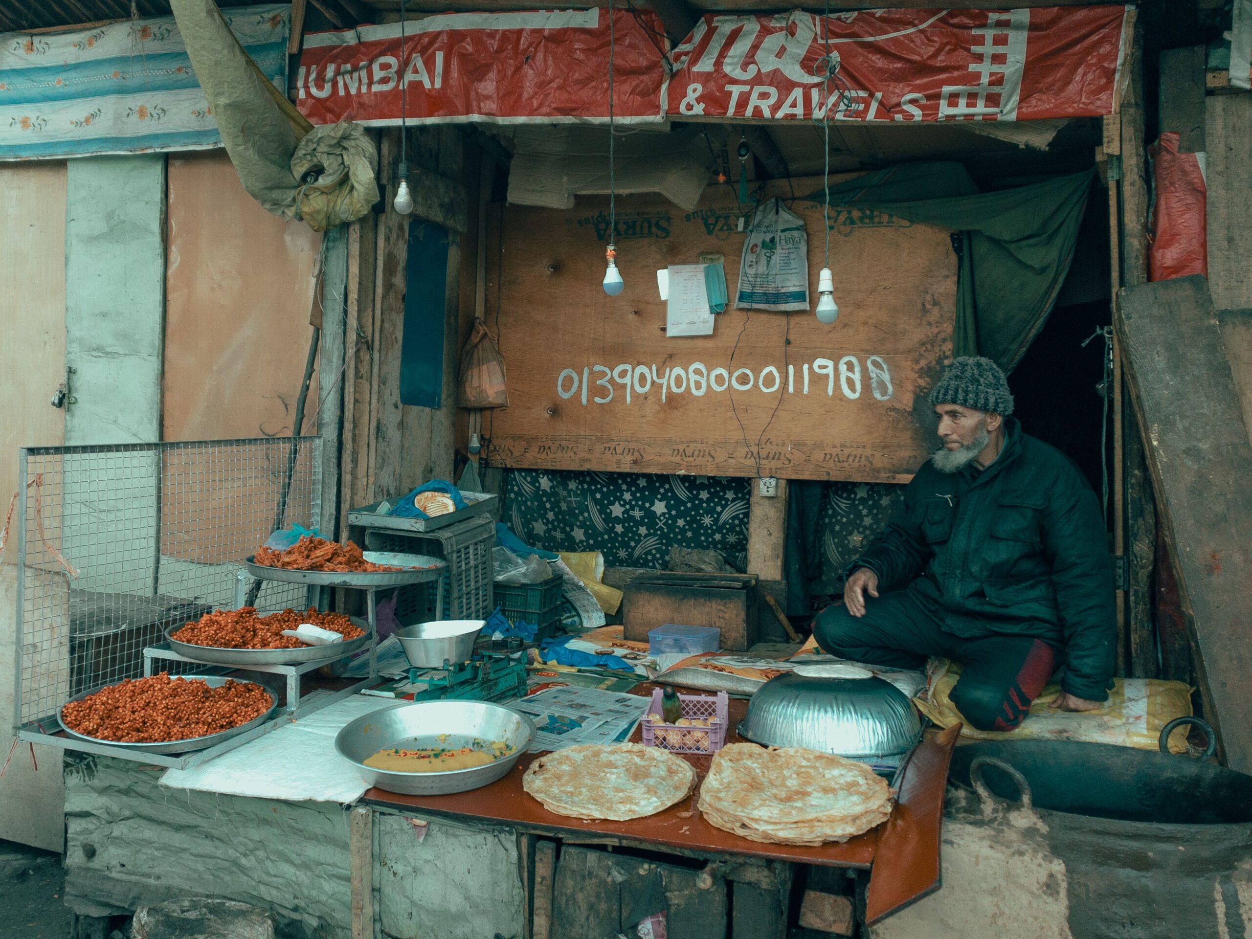 Elderly street food vendor sitting at a local stall in Shimla, surrounded by parathas, spicy snacks, and traditional cooking utensils