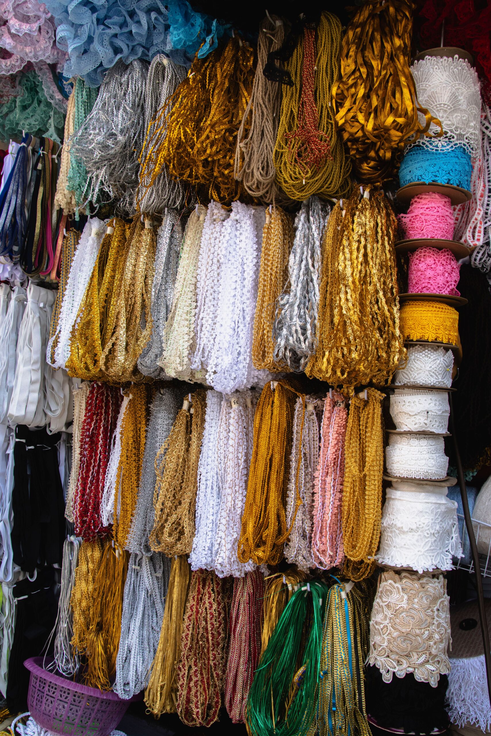 Display wall hanging with various metallic gold, silver, lace, and decorative borders on spools and hanks in a haberdashery shop.